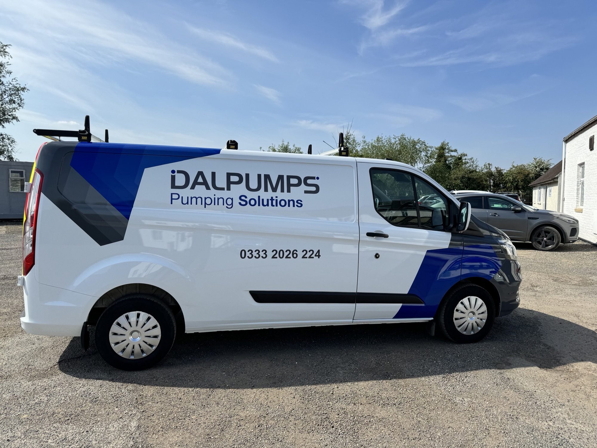 a white and blue van with "dalpumps" printed on the side in a car park. the sky is blue and bright